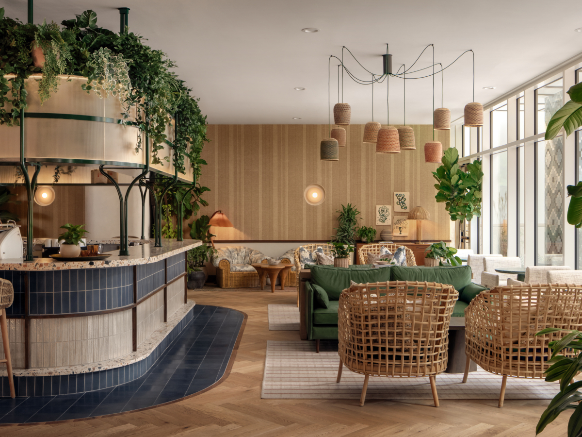 Cozy café interior with natural light, featuring wicker furniture, green plants, a curved tiled counter, and pendant lights—a perfect paseo spot with earthy tones and contemporary decor for a warm and inviting atmosphere.