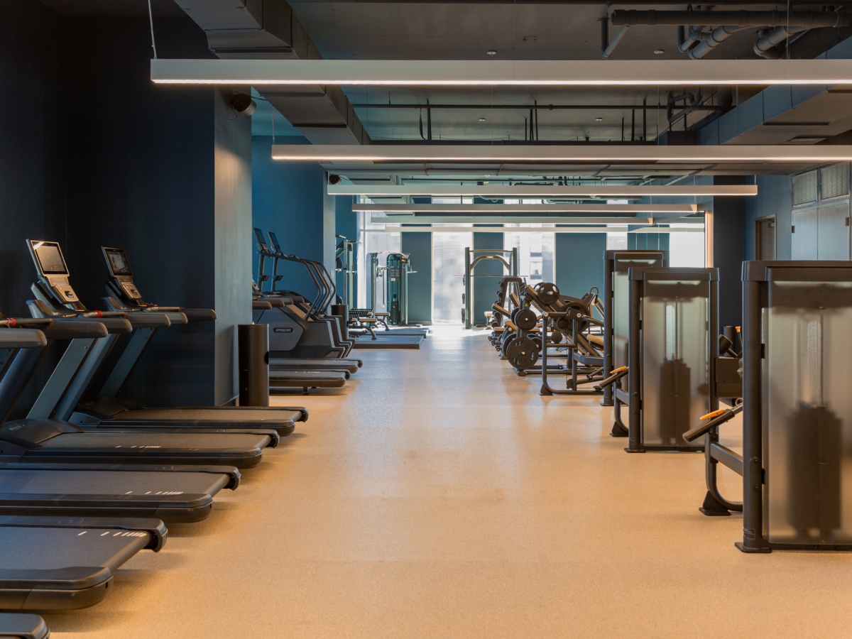A modern, spacious gym along the Paseo, with treadmills on the left, weight machines on the right, and free weights in the back—all well-lit with natural and artificial lighting.