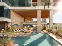 A modern rooftop pool area at Paseo with lounge chairs, blue umbrellas, lush plants, and sweeping city views. The space features wood accents, large windows, and glass railings, with sunlight streaming in from the right.