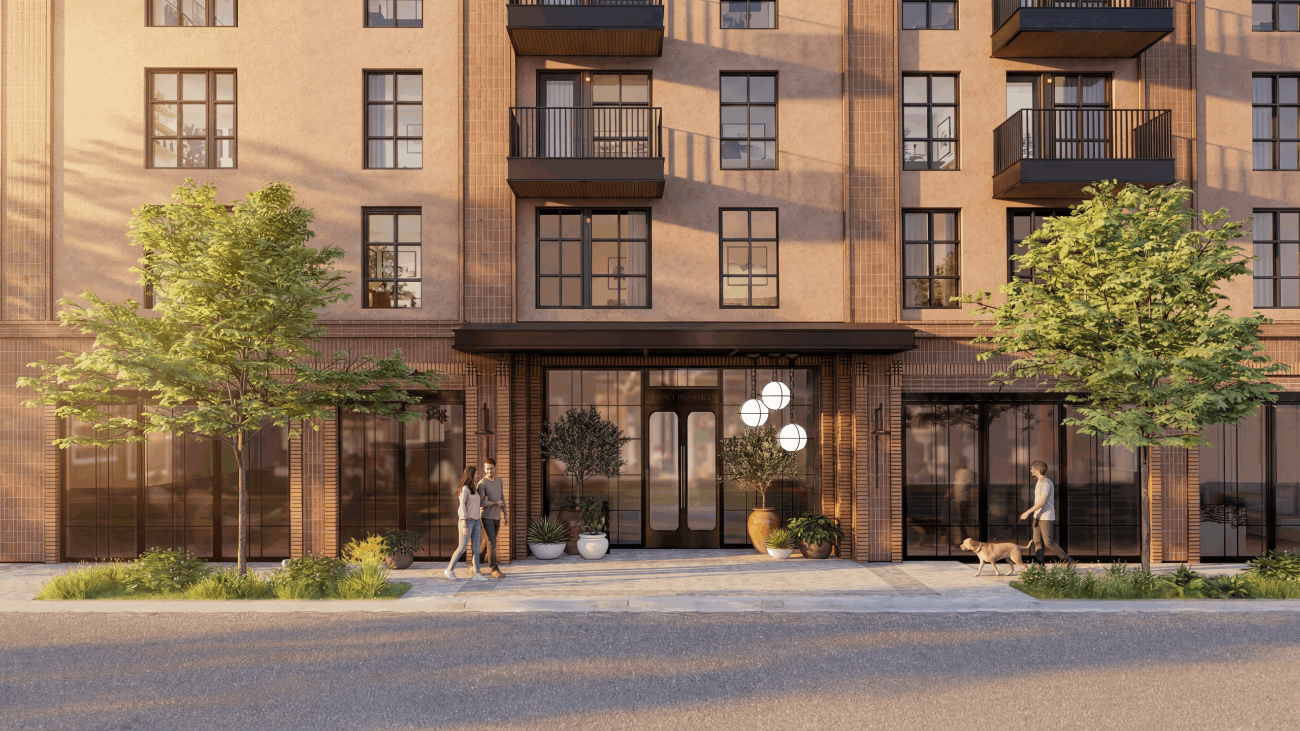 A modern apartment building facade with large windows, balconies, and a main entrance on East 5th St. Two people walk on the sidewalk—one with a dog—surrounded by greenery and potted plants, in warm afternoon light.
