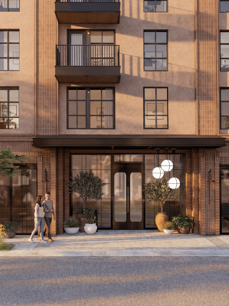 A modern apartment building facade with large windows, balconies, and a main entrance on East 5th St. Two people walk on the sidewalk—one with a dog—surrounded by greenery and potted plants, in warm afternoon light.