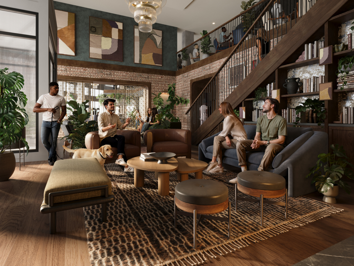 A cozy, modern lounge at Rambler Riverfront with five people and a dog, featuring a staircase, bookshelves, abstract artwork, large windows, plants, and warm lighting. Some people are chatting while others sit quietly.