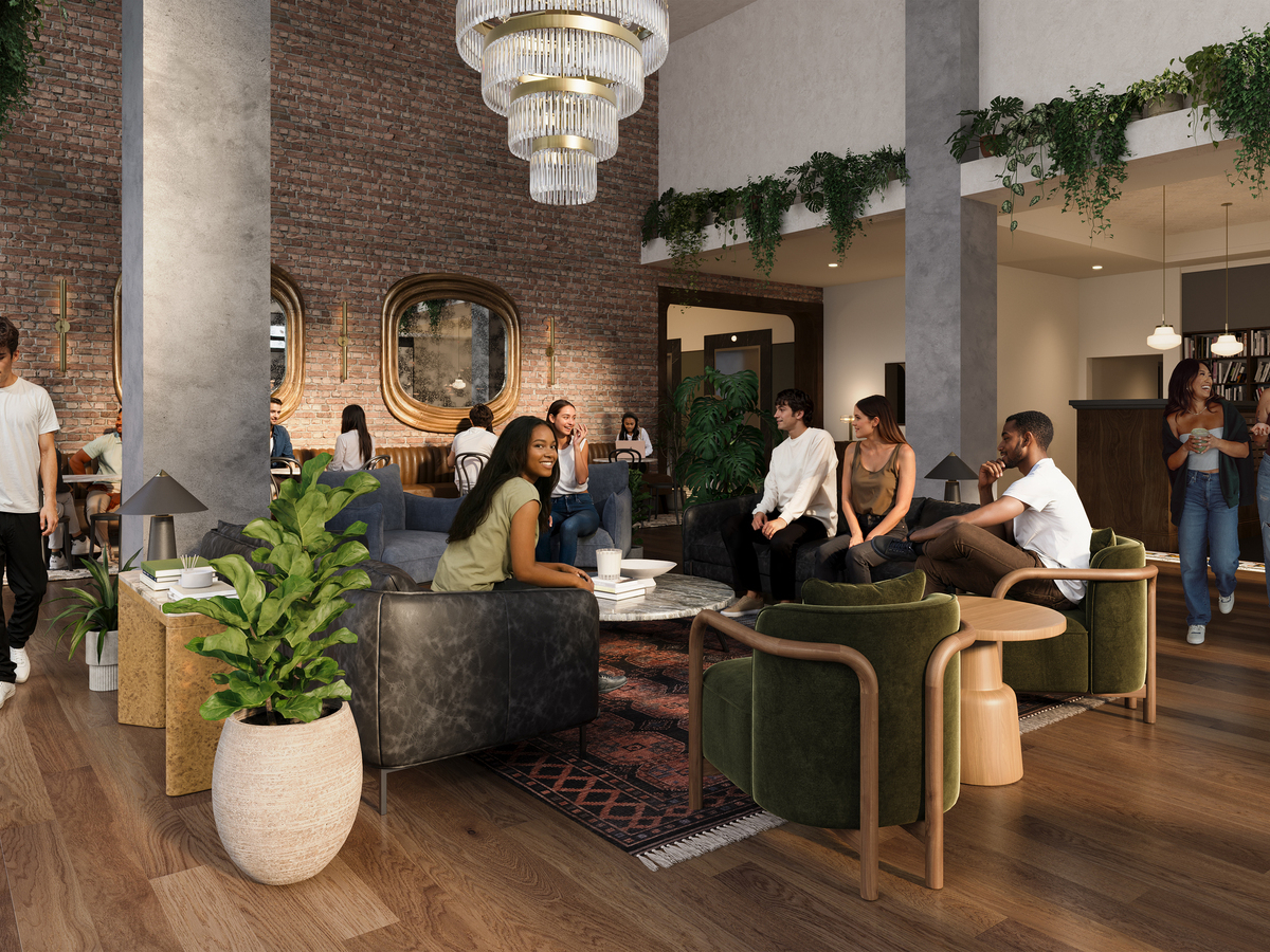 A modern lounge at Rambler Riverfront with people socializing on sofas and chairs. The room features wooden floors, plants, hanging lights, brick walls, large mirrors, and a man walking a dog on the left side.