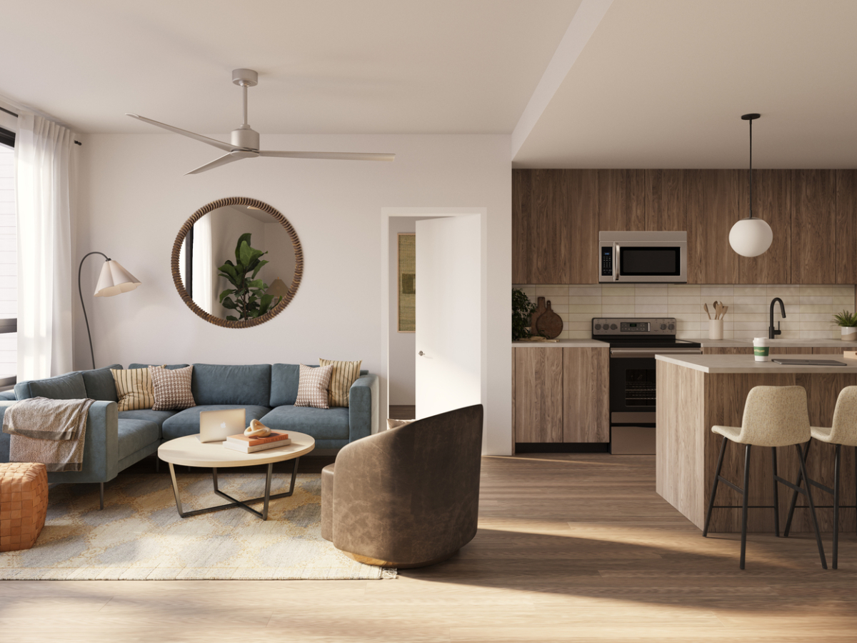 Modern open-plan living room and kitchen in a Rambler Riverfront style, featuring wooden floors, a blue sectional sofa, round mirror, cozy decor, pendant lights above the kitchen island, and a large window letting in natural light.