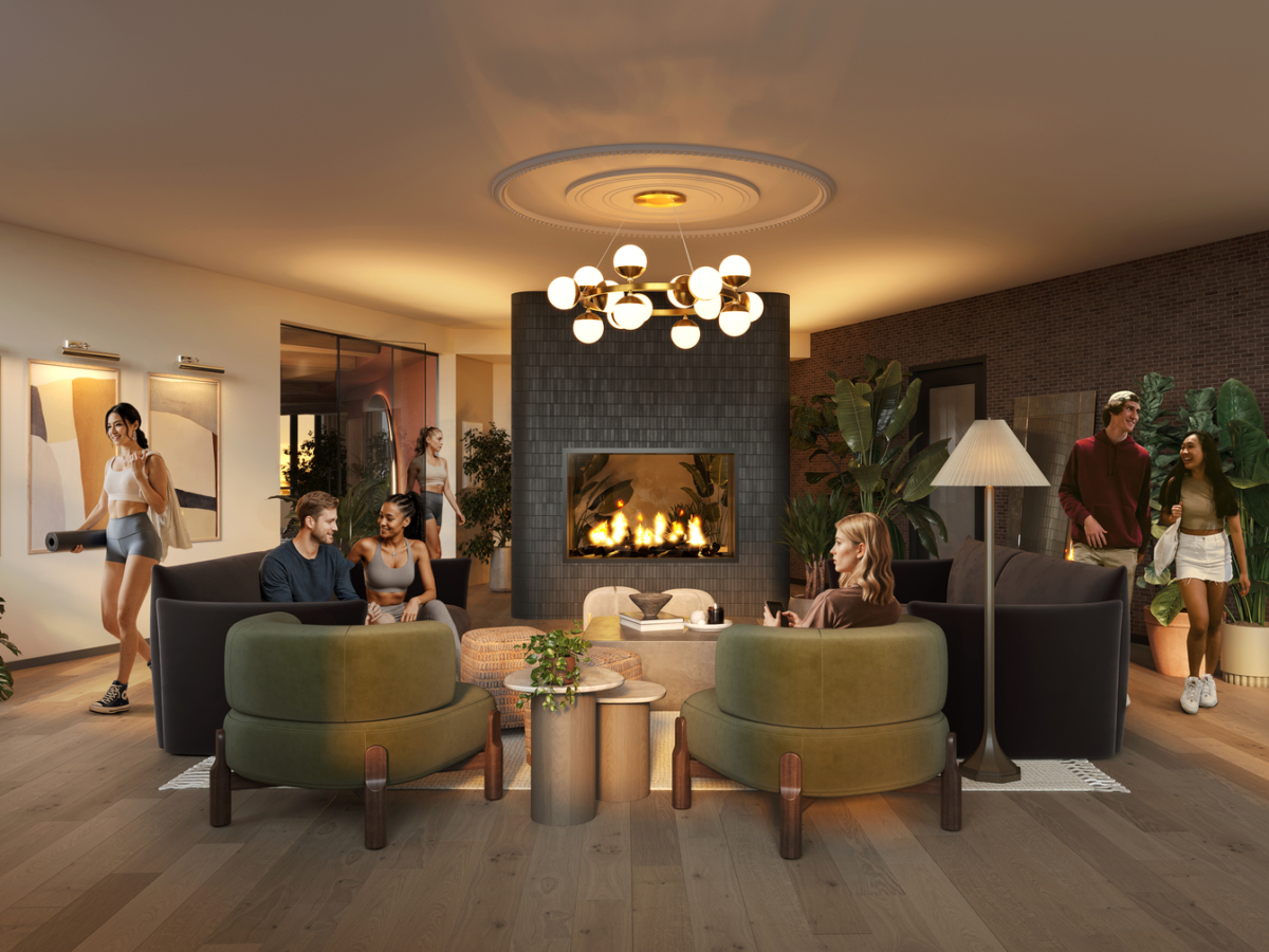 A modern lounge at Rambler Riverfront features a central fireplace, cozy seating, stylish lighting, plants, and art on the walls. Several people relax, chat, or walk through the warm, inviting space.