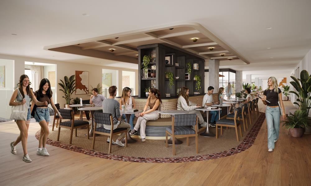 A modern, well-lit café with groups of people sitting and chatting at round tables. A server walks toward a table, and two women walk together, smiling. The space has wooden floors, plants, and contemporary decor.