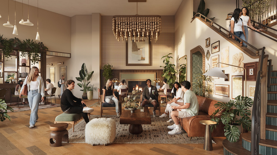 A stylish lounge at Rambler Blacksburg student housing with people sitting, chatting, and relaxing. Warm lighting, modern furniture, plants, and art on the walls create a cozy atmosphere. Some people stand near the stairs while others are seated on couches and chairs.
