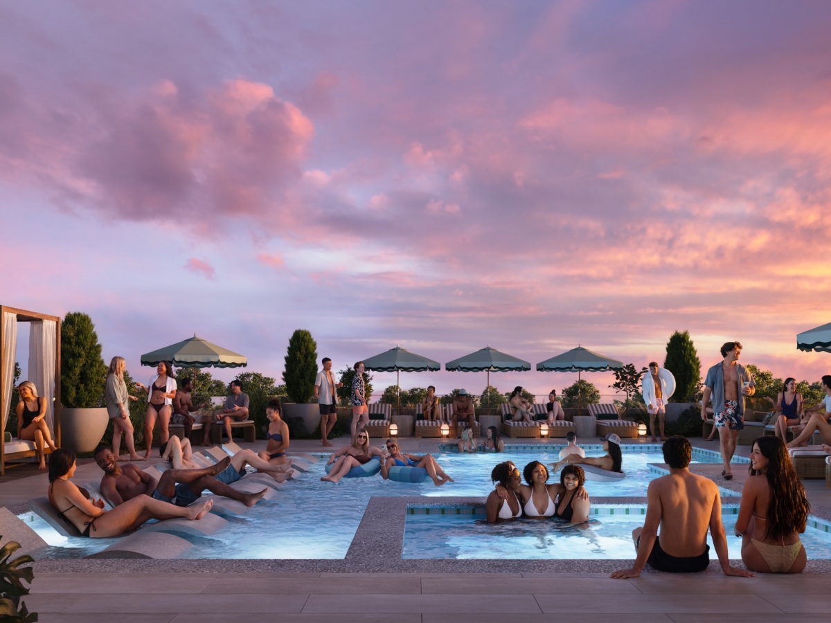 People relax in and around a rooftop pool and hot tub at sunset at Rambler Blacksburg student housing. Some are sitting on loungers under umbrellas, while others are in the water or socializing. The sky is colorful with clouds, and the atmosphere is lively.