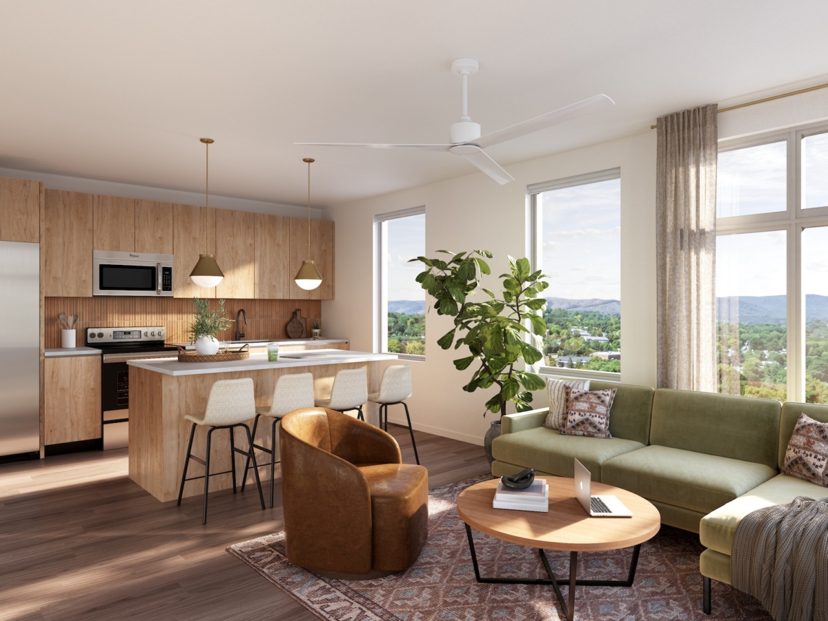 Modern, sunlit Rambler Blacksburg student housing apartment with wood floors, green sofa, round coffee table, leather chair, large windows, kitchen with island, barstools, stainless steel appliances, and indoor plant.