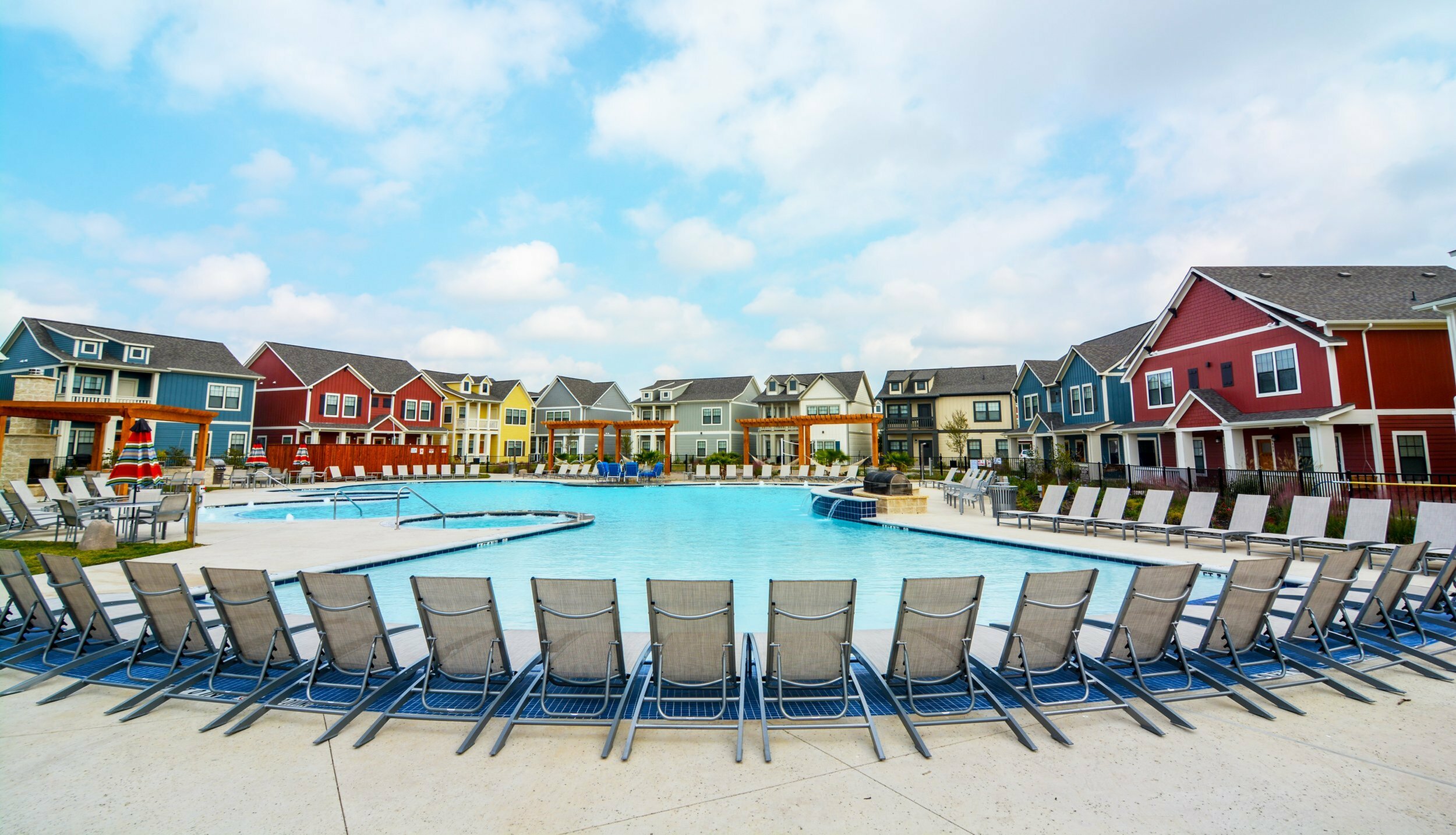 A pool with chairs and a row of houses.