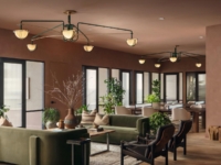 Modern lounge with green sofas, armchairs, plants, and large windows. Overhead light fixtures hang from the ceiling. A blue abstract painting is on the right wall, and a central coffee table holds vases and books.