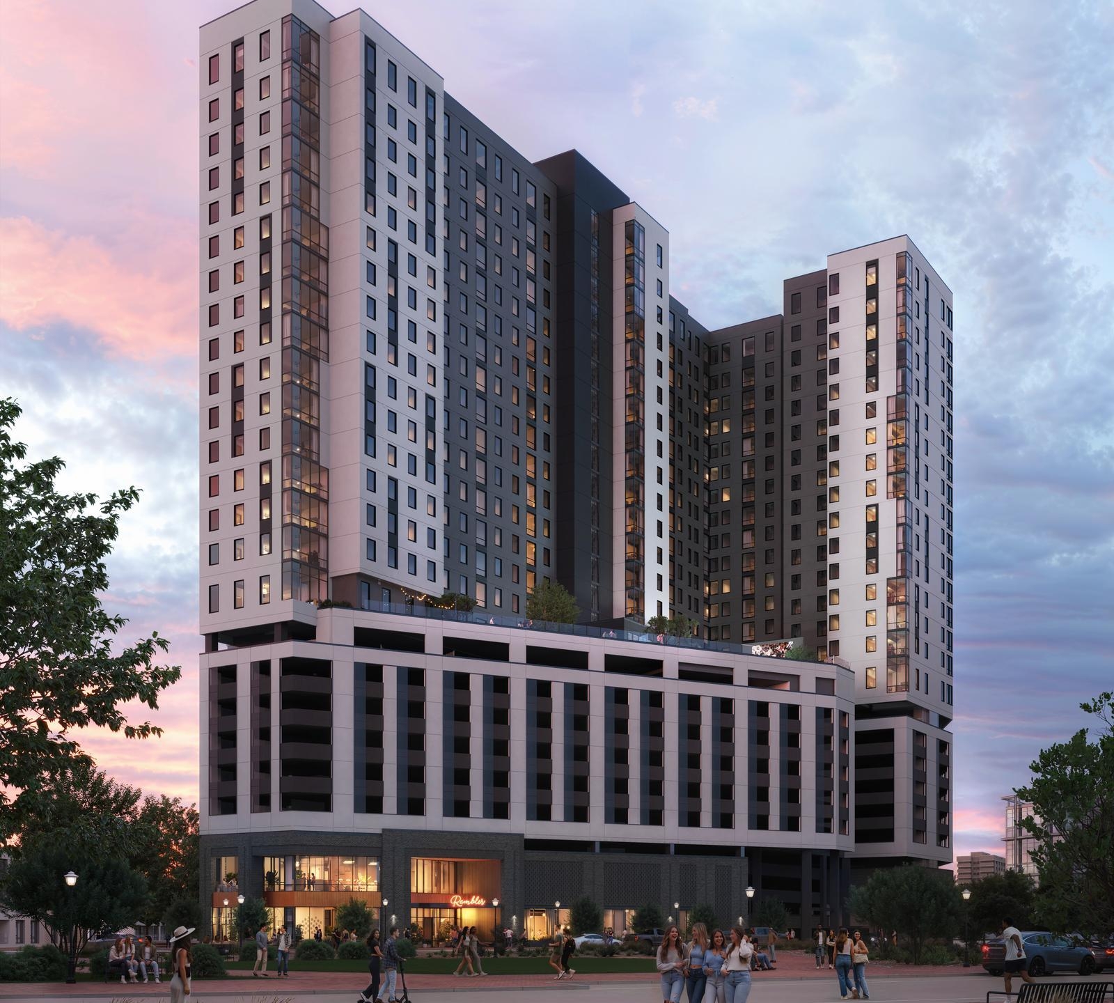 A modern high-rise Gainesville student housing apartment building at sunset, featuring large windows, a multi-story base, rooftop greenery, and people gathering in the lively plaza below among trees and lampposts.