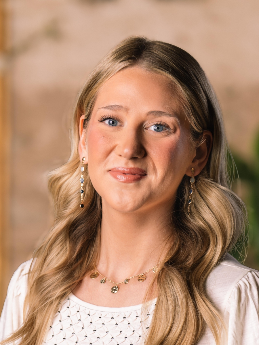Annabella Tuck, a smiling woman with blonde hair, wearing a necklace with circular gold charms and drop earrings.