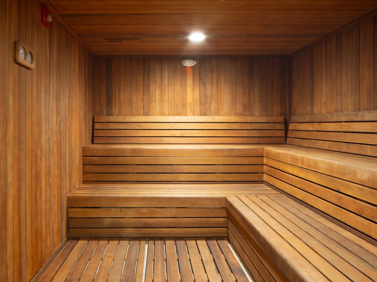 An empty wood-paneled sauna room with multi-level bench seating and a wall-mounted gauge, shown in the before and after rambler college park south transformation.