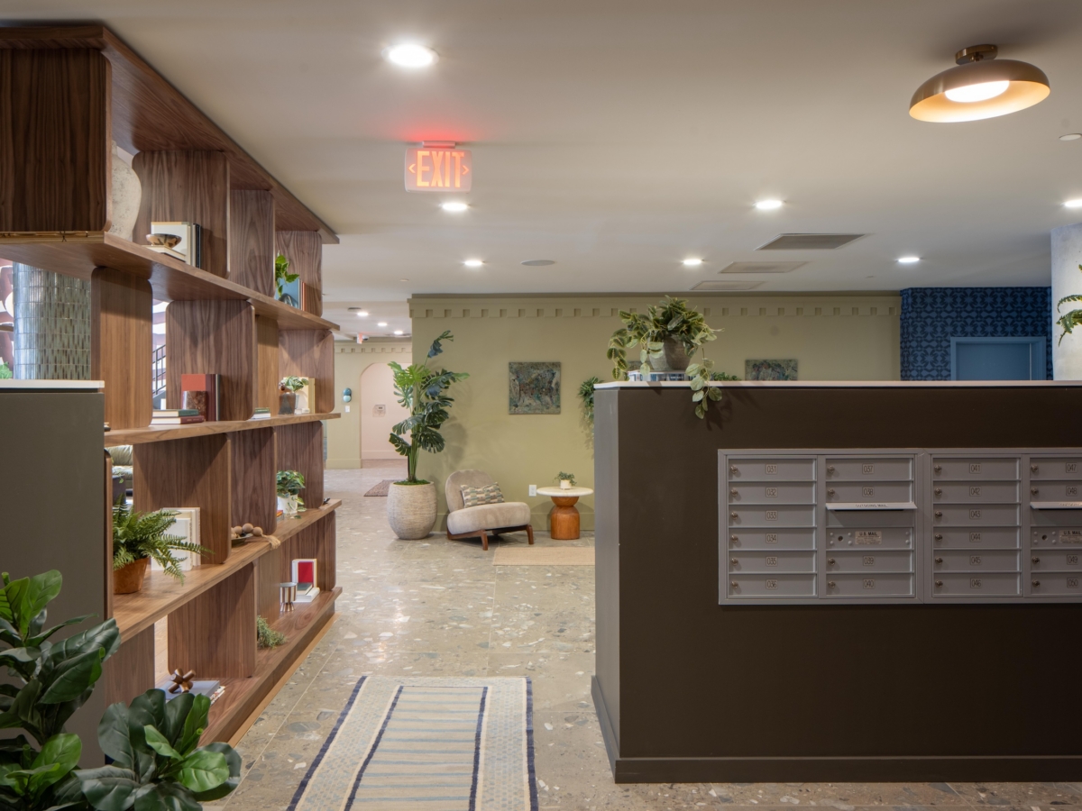 Lobby area with a wood bookshelf, a wall of metal mailboxes, and a seating area with an armchair and side table, shown after the Rambler College Park South renovation.