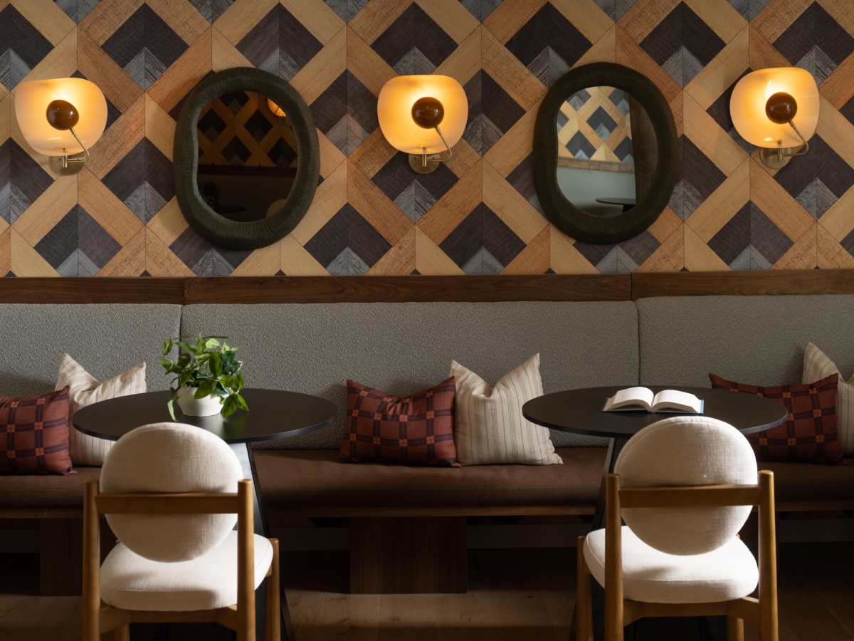 Two round tables with chairs in front of a long cushioned bench, featuring wall-mounted sconces and two mirrors against a geometric patterned wall in the Rambler College Park South.