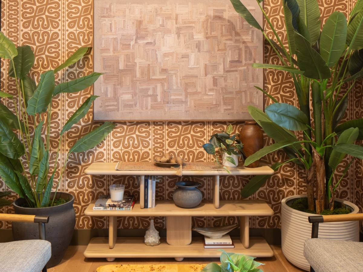 A sitting area with patterned wallpaper, a light wood console table, and textured art, shown here in a before and after Rambler College Park South update, with potted plants and a coffee table holding open books in the foreground.
