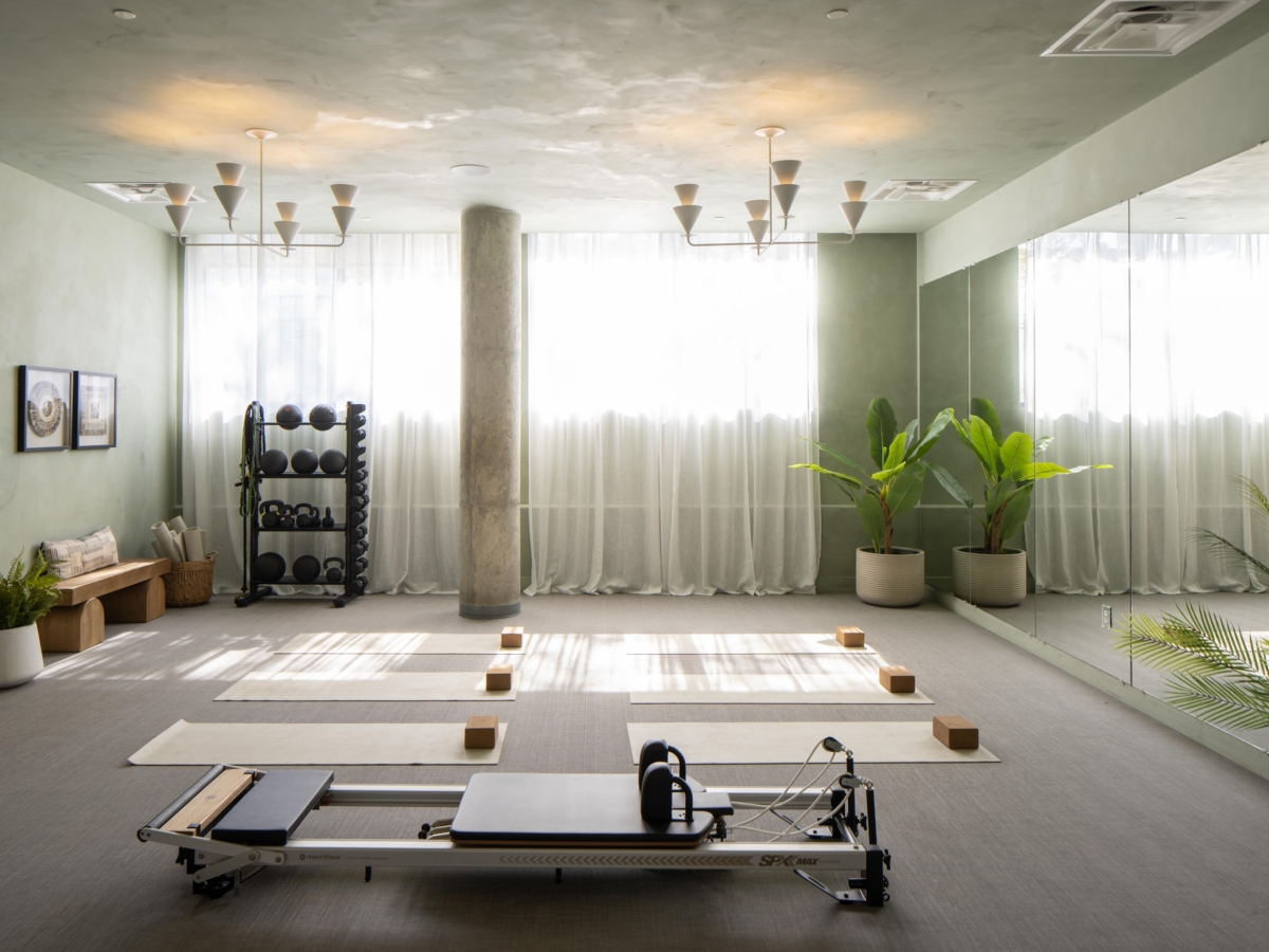 A bright pilates studio featuring a reformer machine, yoga mats, and a kettlebell rack by sheer-curtained windows, a transformation similar to a before and after at Rambler College Park South.