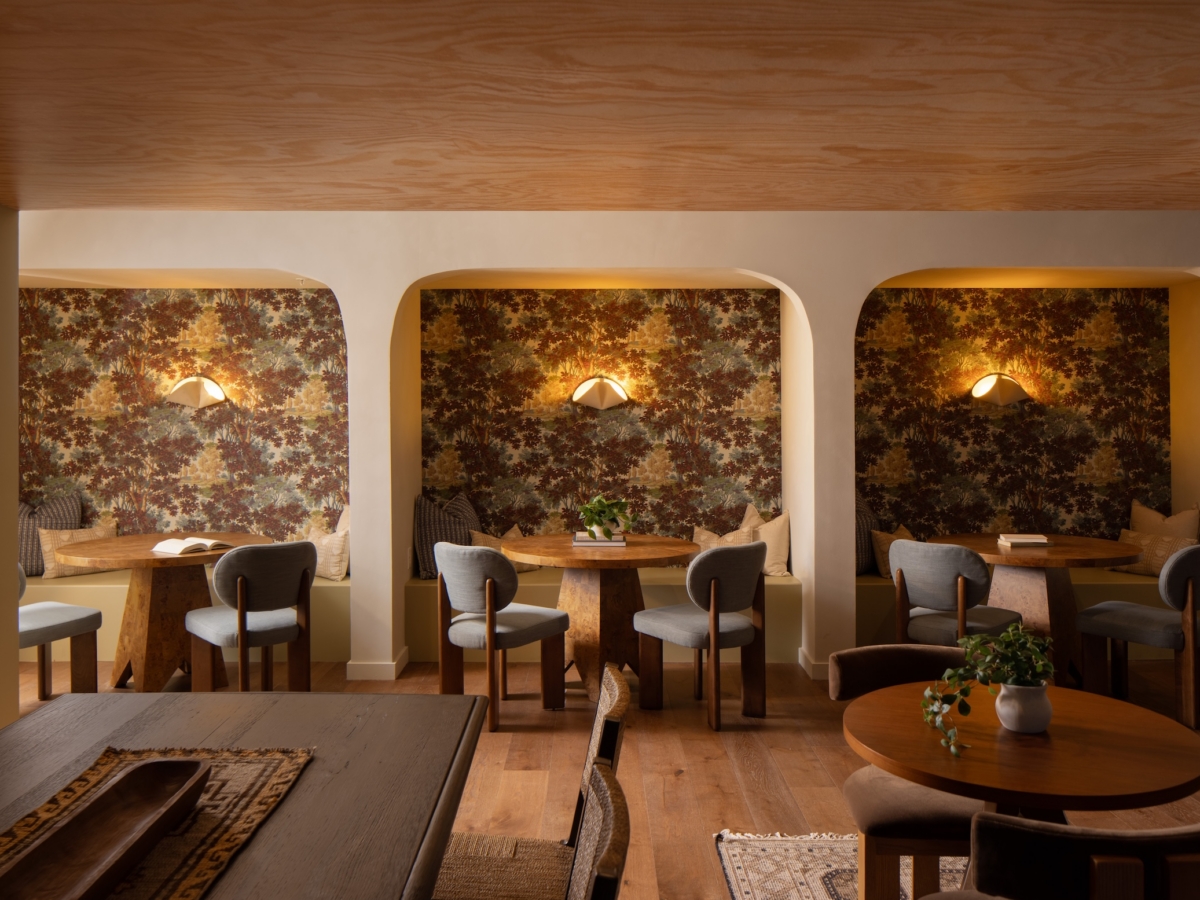 Three arched alcoves with patterned wallpaper at Rambler College Park South, each featuring a round wooden table, two chairs, and a wall-mounted light.