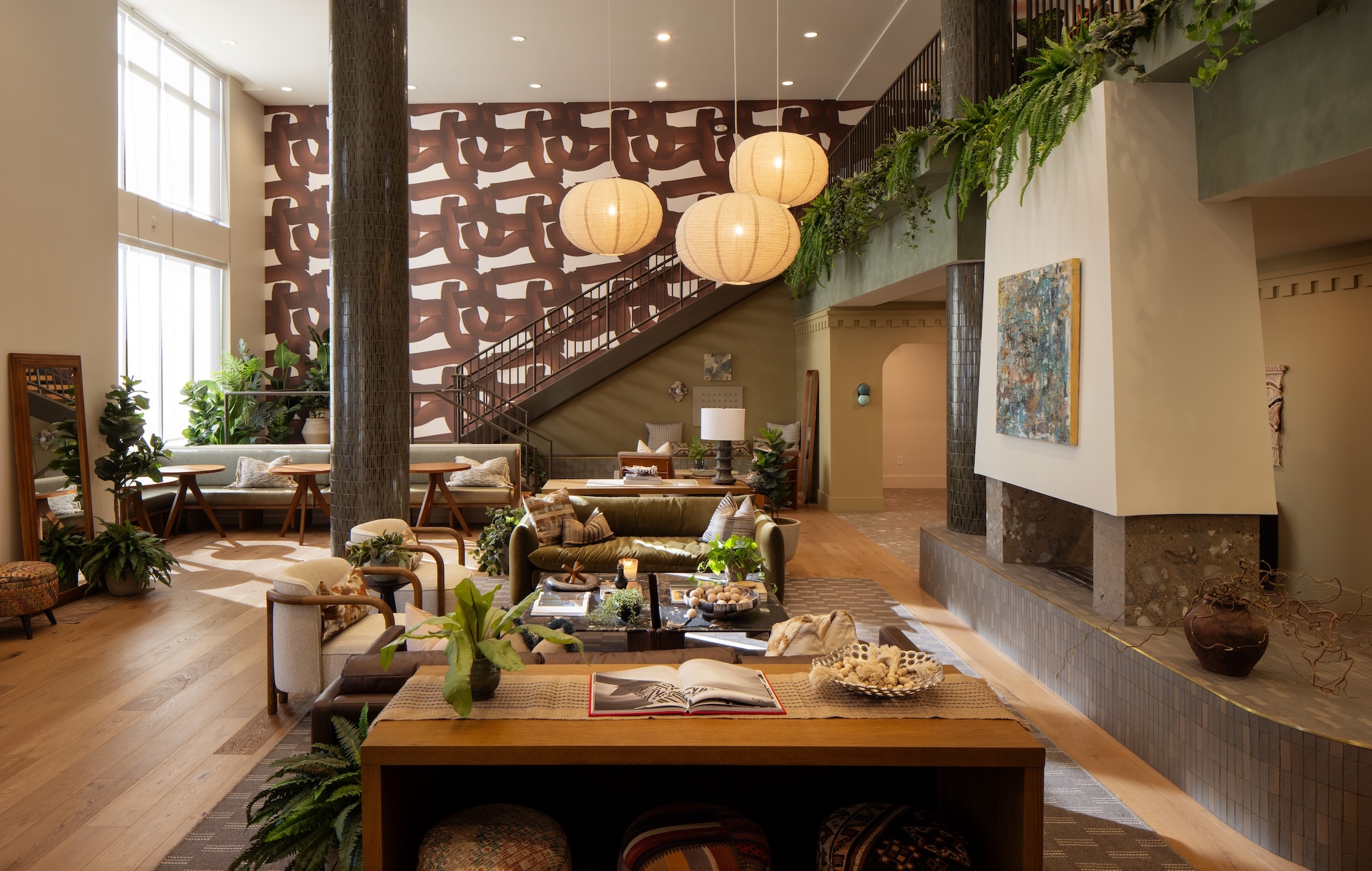 A spacious lobby lounge at the Rambler College Park South, featuring a central fireplace, multiple seating areas with sofas and chairs, and a staircase leading to an upper level.